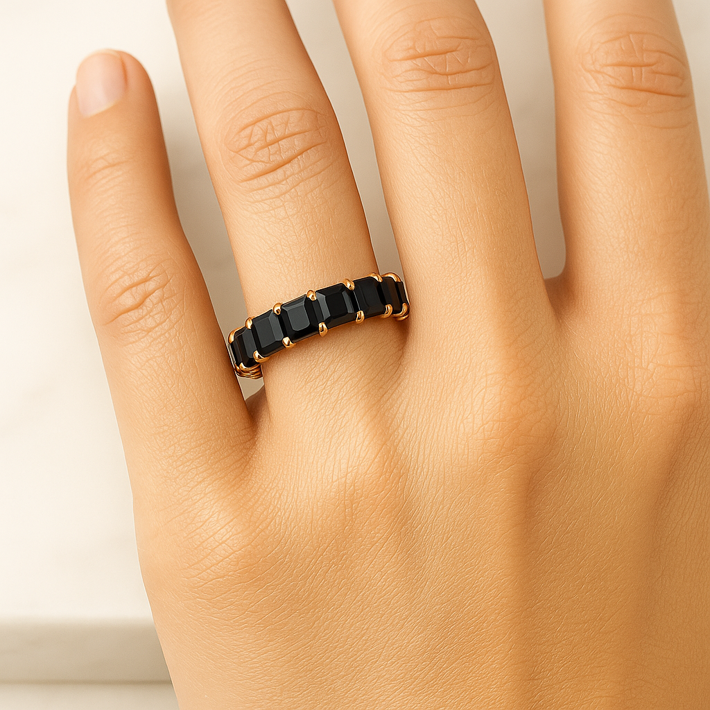 Gold ring with black stones on a hand against a neutral background